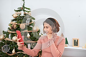 Funny asian girl taking selfie pictures on smartphone camera at home near Christmas tree