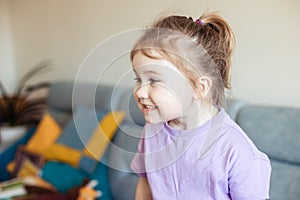 Funny Asian little girl laughing and looking away while sitting on the couch in her house. Close up, copy space