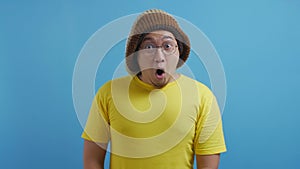 Funny Asian man with open mouth and big eyes, shocked surprised wow expression. Stunned amazed gesture over blue background