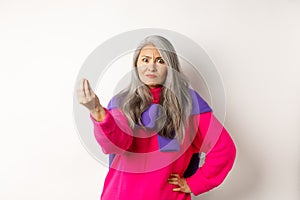Funny asian woman staring angry and confused, shaking fingers, standing grumpy against white background