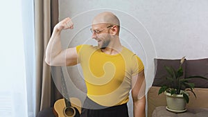 Funny athletic nerdy man with glasses looks at the camera, smiles stupidly, shows a pumped bicep and moves his eyebrows