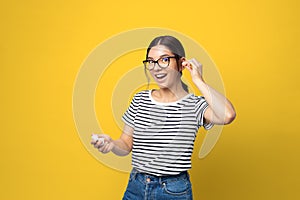 Funny attractive multi ethnicity young woman with glasses using in-ears wireless headphones against yellow background