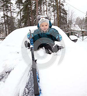 Funny baby boy cleans car bonnet from snow