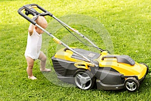 Funny baby boy cuts the lawn with a grassmower