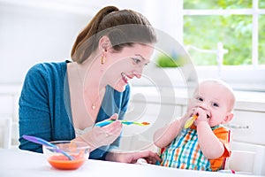 Funny baby boy eating his first solid food with his mother