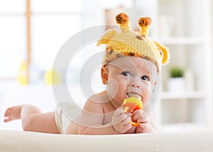 Funny baby boy in giraffe hat lying on his belly in nursery. Little kid using nibbler toy. photo