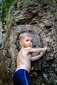 Funny baby boy hiker climbing on natural mountain cliff enjoying summer travel vacation