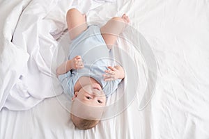 Funny baby boy lying on bed at home on white bedding. top view.