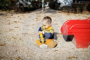 Funny baby boy playing at outdoors playground. Toddler plays with toy car. Fine sunny day