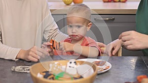 funny baby boy tasting orange homemade cookie sitting kitchen table two female mother celebrating halloween holiday