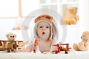 Funny baby boy weared pilot hat with wooden airplane and teddy bear toys