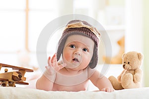 Funny baby boy weared pilot hat with wooden airplanes and teddy bear toys