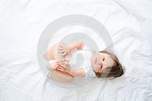 funny baby boy in white bodysuit smiling and lying on a white bedding at home. top view.