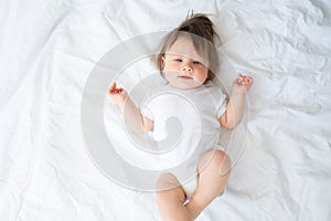 funny baby boy in white bodysuit smiling and lying on a white bedding at home. top view.