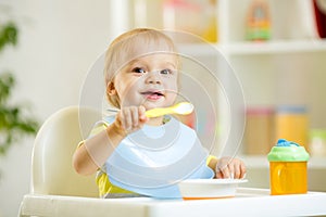 Funny baby child boy eating itself with spoon in