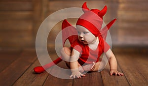 Funny baby in devil halloween costume on wooden background