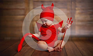 Funny baby in devil halloween costume on wooden background