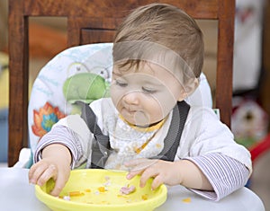 Funny baby eating with hands from plate