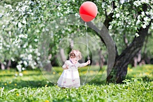 Funny baby girl in apple tree garden with red ballon