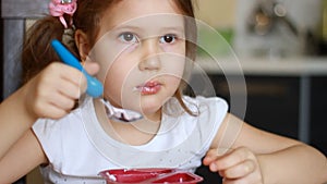 Funny baby girl eating with enjoyment cottage cheese in the kitchen. Portrait of a child eating yogurt for breakfast.