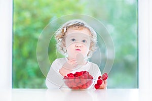 Funny baby girl eating raspberry at white table