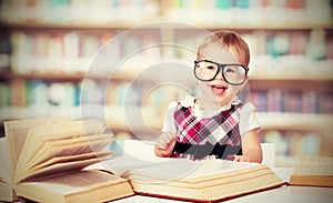 Funny baby girl in glasses reading book in library