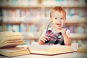 Funny baby girl in glasses reading a book in a library