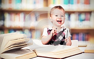 Funny baby girl in glasses reading a book in a library