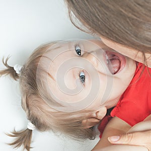 Funny baby girl lying near happy mother on white bed