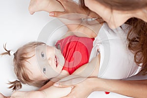 Funny baby girl lying near happy mother on white bed