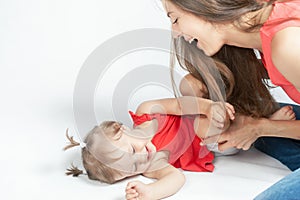 Funny baby girl lying near happy mother on white bed