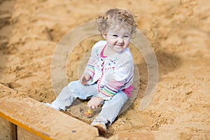 Funny baby girl playing with sand on a playground