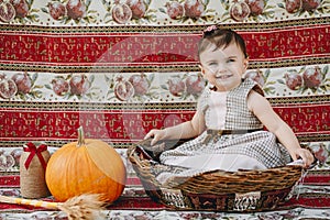 Funny baby girl sitting in big straw basket and laughing next to the pumpkin