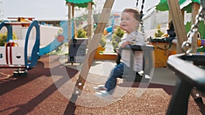 Funny baby girl swinging on a swing at the playground. Outdoor. Real time. Side view. Concept of children's autism