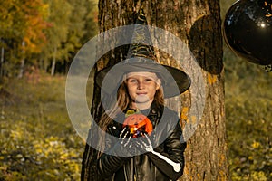 Funny baby girl in a witch costume for Halloween with black and orange balloons.