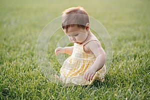 Funny baby kid. Cute adorable baby girl in yellow dress sitting on grass in park outdoor. Funny child toddler playing and having