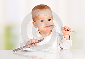 Funny baby with a knife and fork eating food