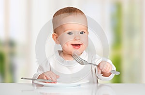 Funny baby with a knife and fork eating food