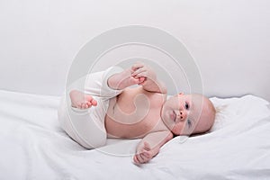 Funny baby lying down on white sheet. Newborn lying on side and smiling photo