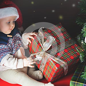 Funny baby opening gift box at Christmas. Dressed Santa hat