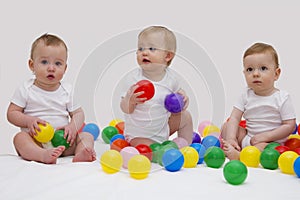 Funny baby triplets smiliing and playing with colorful balls. Studio shot