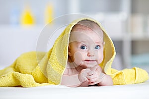 Funny baby under soft towel. Cute child lying on bed after bathing in living room