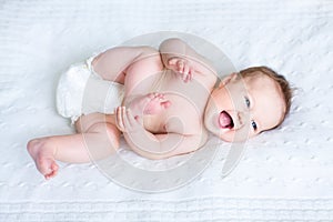 Funny baby wearing diaper playing with her feet