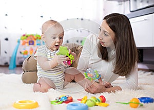 Funny baby and young woman playing in nursery. Happy family having fun with colorful toys at home.