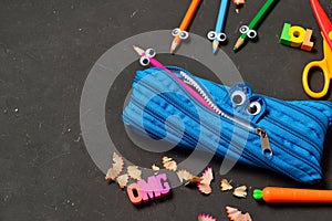 Funny Back to School concept - pencil case eating pencils on black chalk background. Space for text