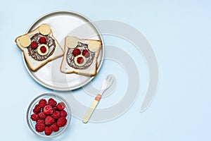 Funny bear face sandwich toast bread with peanut butter, cheese and raspberry on plate blue background copy space. Kids