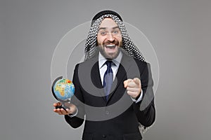 Funny bearded arabian muslim businessman in keffiyeh kafiya ring igal agal black suit isolated on gray background