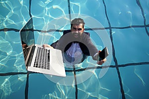 Funny bearded business man in suit using phone and laptop in swimming pool. Concept of young people working mobile