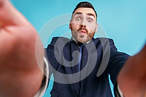 Funny bearded businessman wearing official style suit, taking selfie, looking at camera POV, point