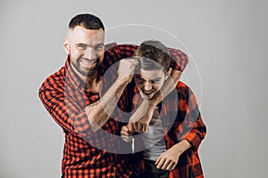 Funny bearded dad and his son fighting on the grey background